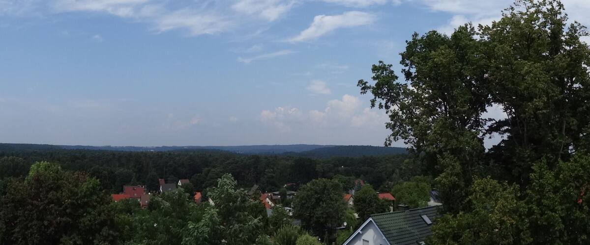 A rural landscape with dense trees, scattered houses, and distant hills under a clear sky.