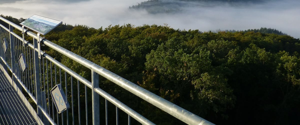 A forested mountain range with a view of mist-covered valleys and a metal observation platform.