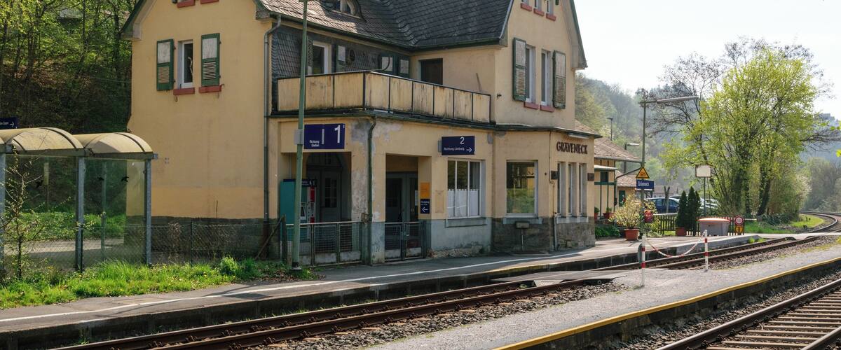 A train station with a yellow building, numbered platforms, and tracks.