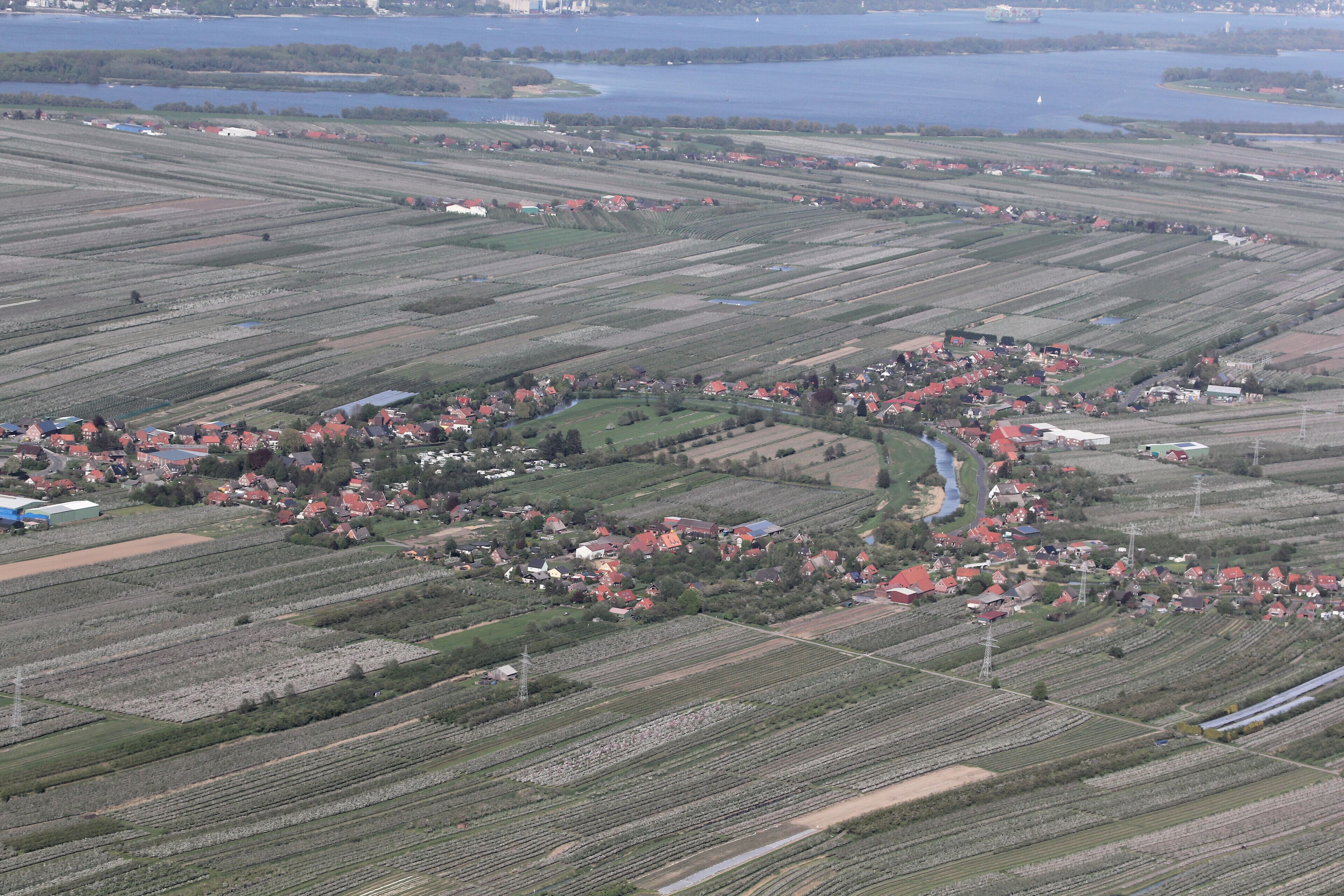 An aerial view of a rural area with fields, a small village, and a lake in the background.