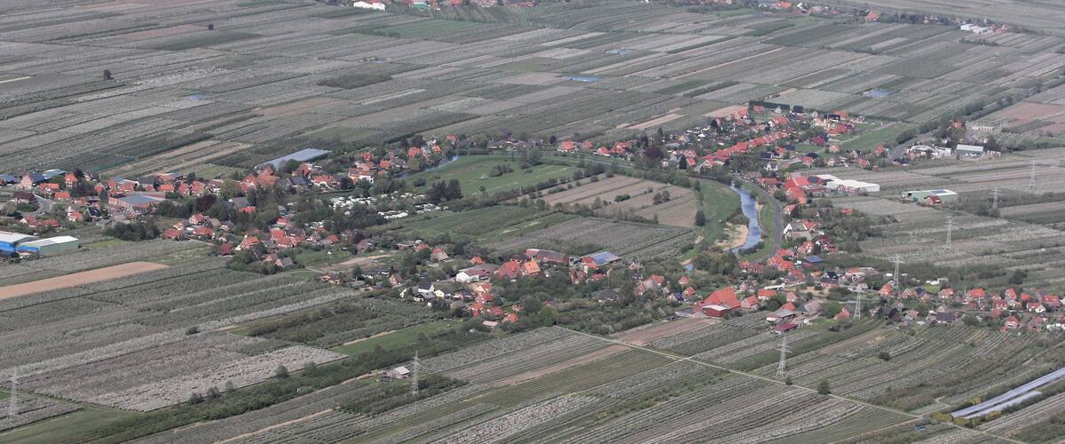An aerial view of a rural area with fields, a small village, and a lake in the background.