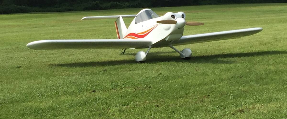 A small white airplane with red and orange accents parked on a grassy field.