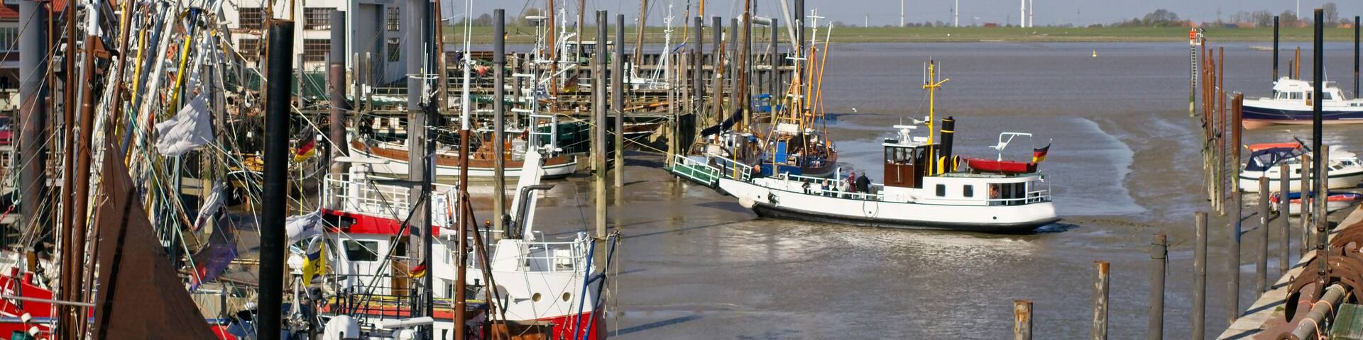 A marina with various boats docked, a river, and wind turbines in the distance.
