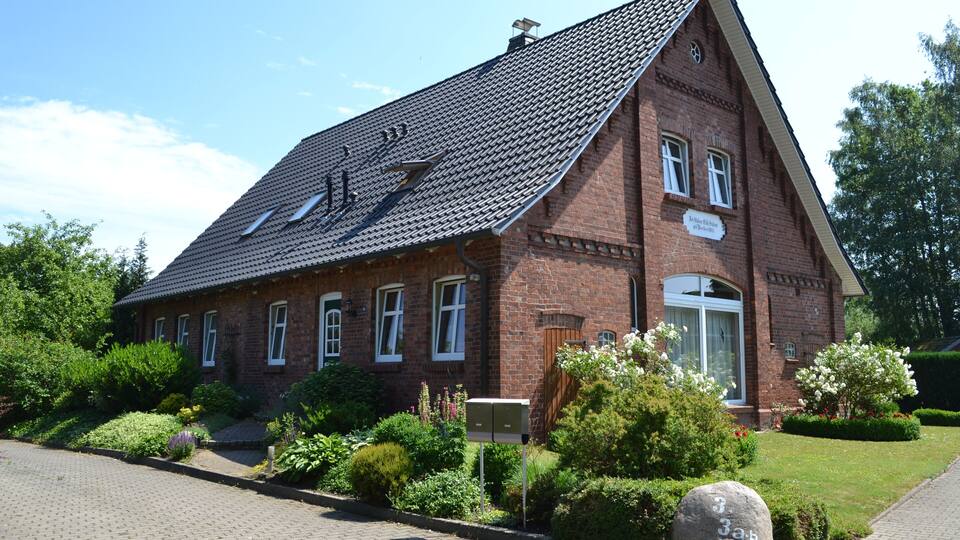 A red brick building with a steeply pitched roof and a small garden in front.
