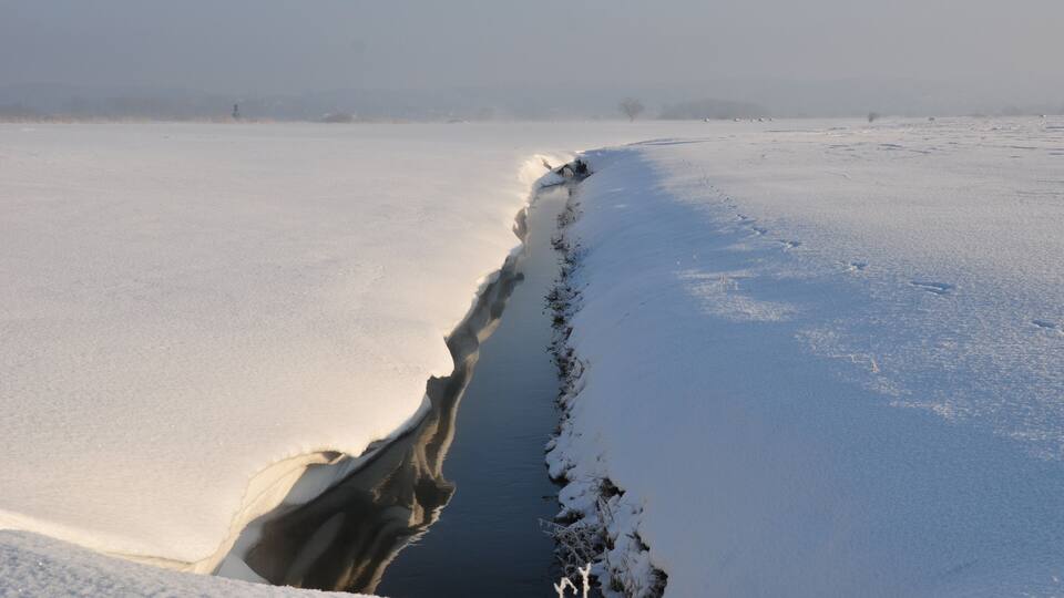 A frozen river with a narrow opening, surrounded by snow-covered landscape.