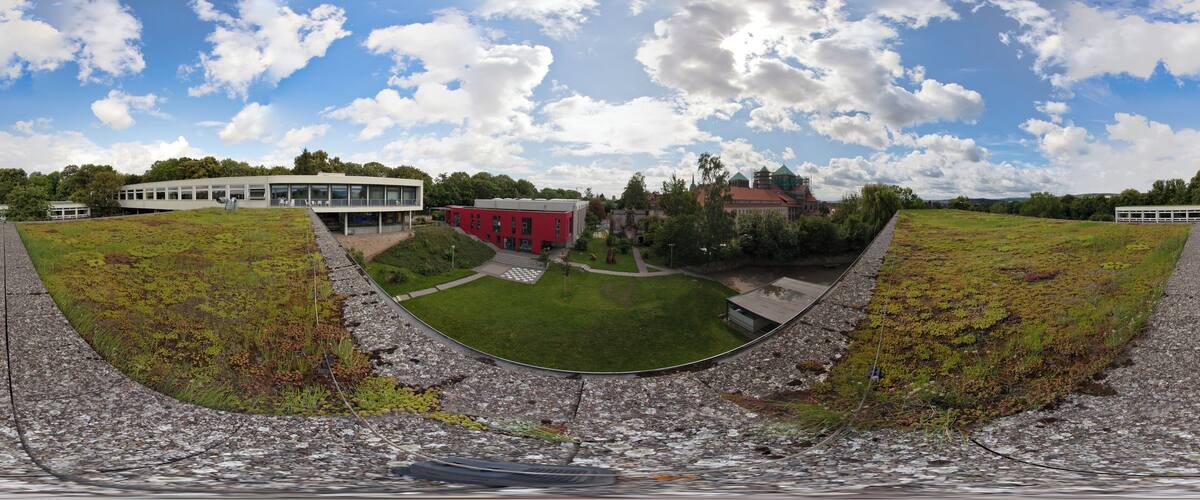 A panoramic view of a coastal landscape with a modern building, a red structure, and a church.