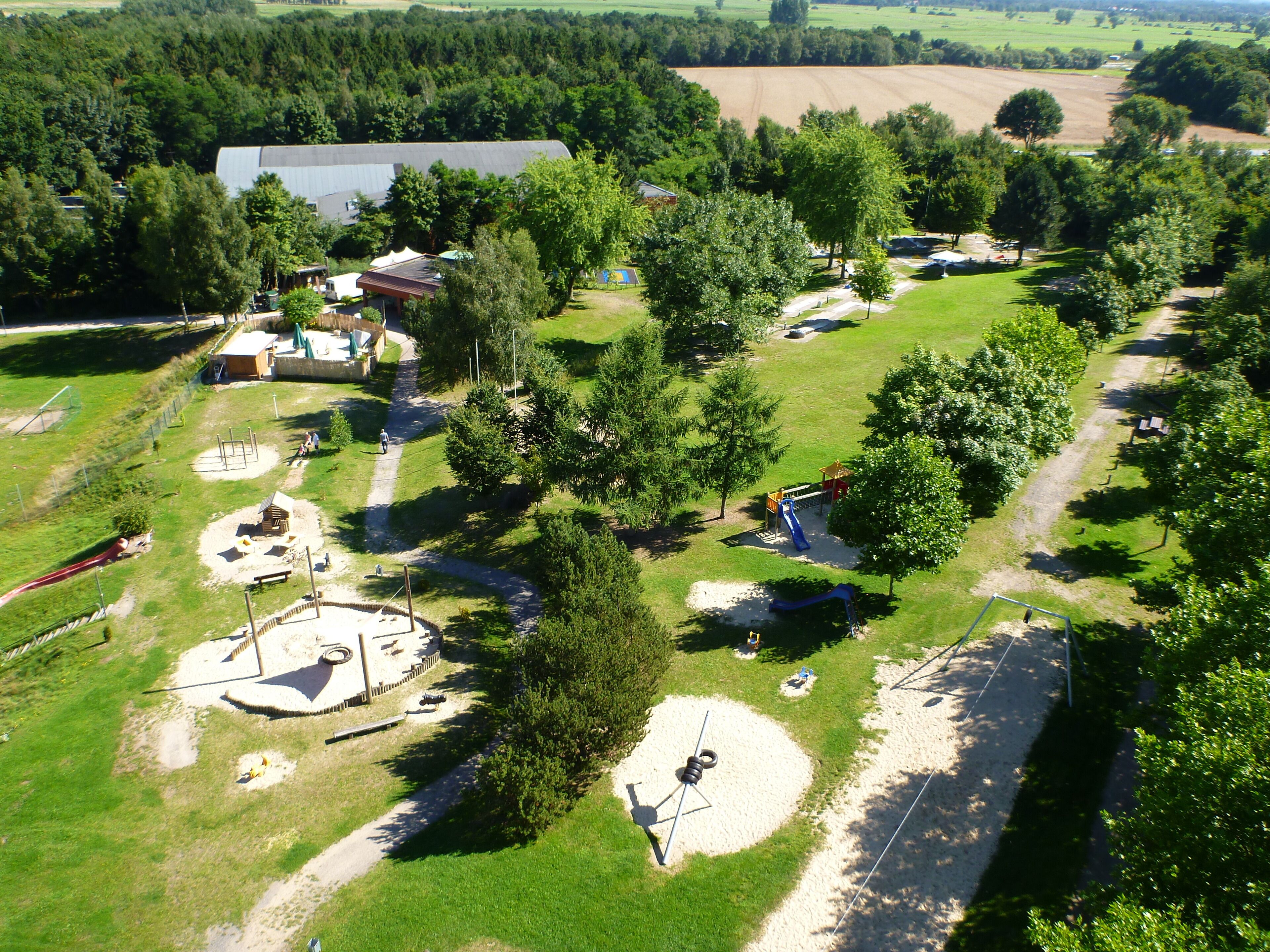 An aerial view of a park with playgrounds, walking paths, and a large barn.