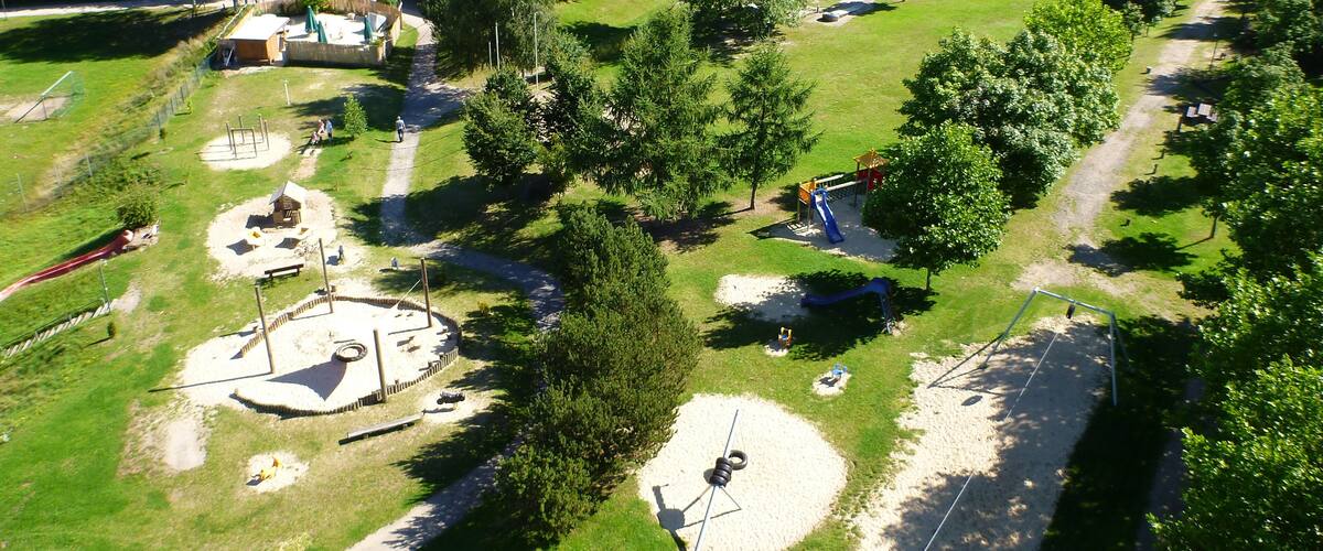 An aerial view of a park with playgrounds, walking paths, and a large barn.