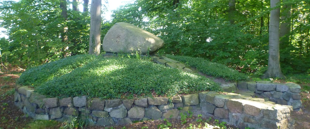 A landscaped garden with a stone wall, a large rock, and surrounding greenery.