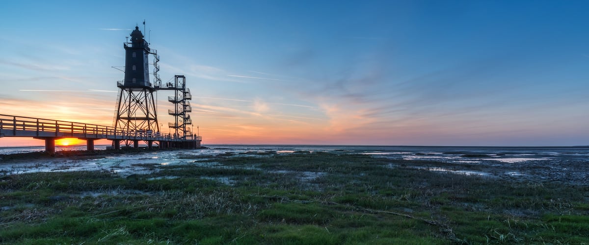 A coastal landscape with a pier and a lighthouse at sunset.