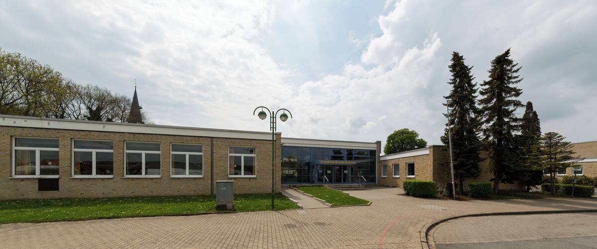 A school building with a brick facade, large windows, and a green lawn.
