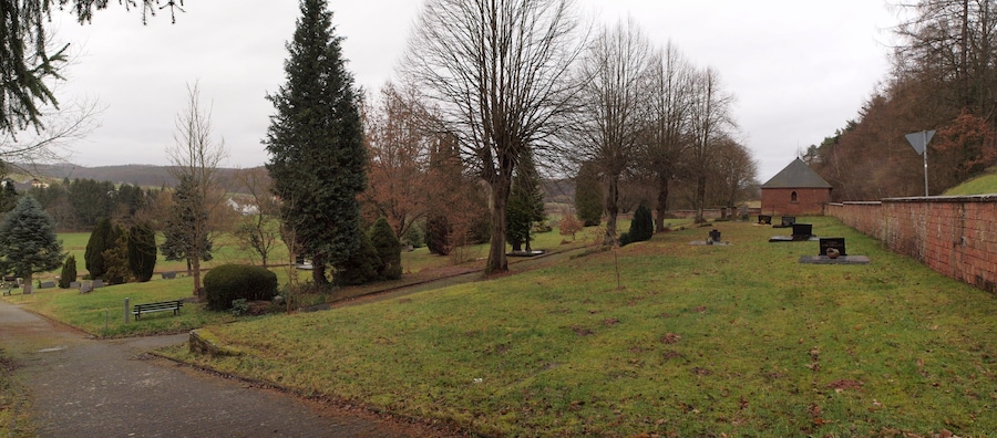 Un cementerio con lápidas, un sendero y una banca.