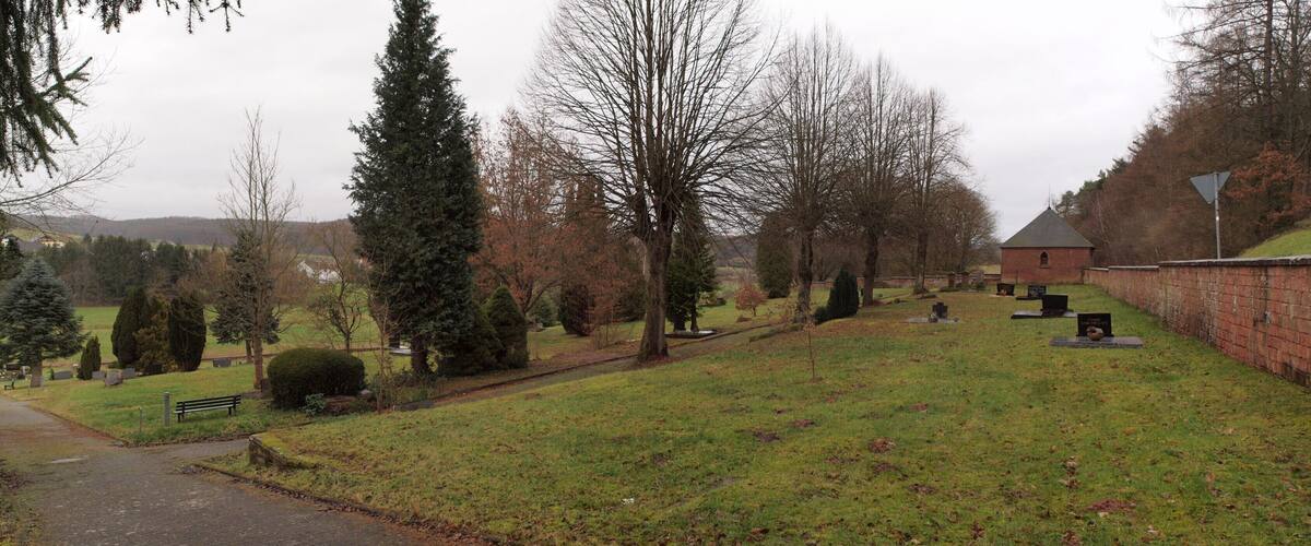 A cemetery with gravestones, a pathway, and a bench.