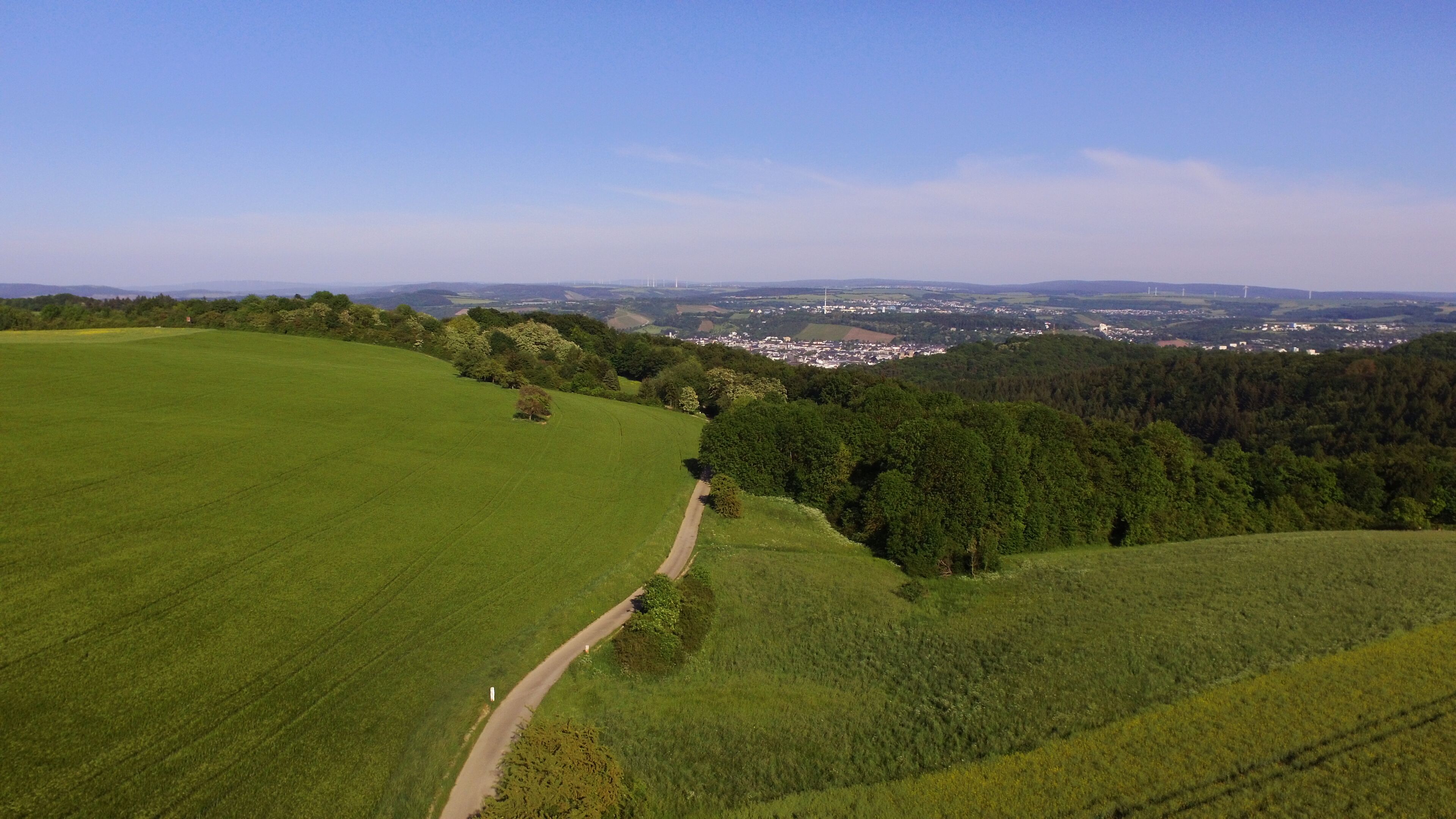 A rural landscape with a winding road, green fields, and a distant town.