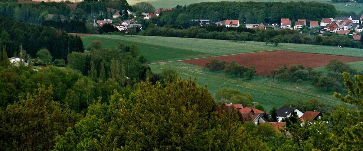 A rural landscape with rolling hills, fields, and scattered houses.