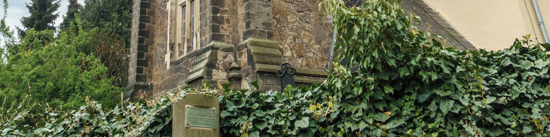 A historic stone tower with a pointed roof, arched windows, and a weather vane.