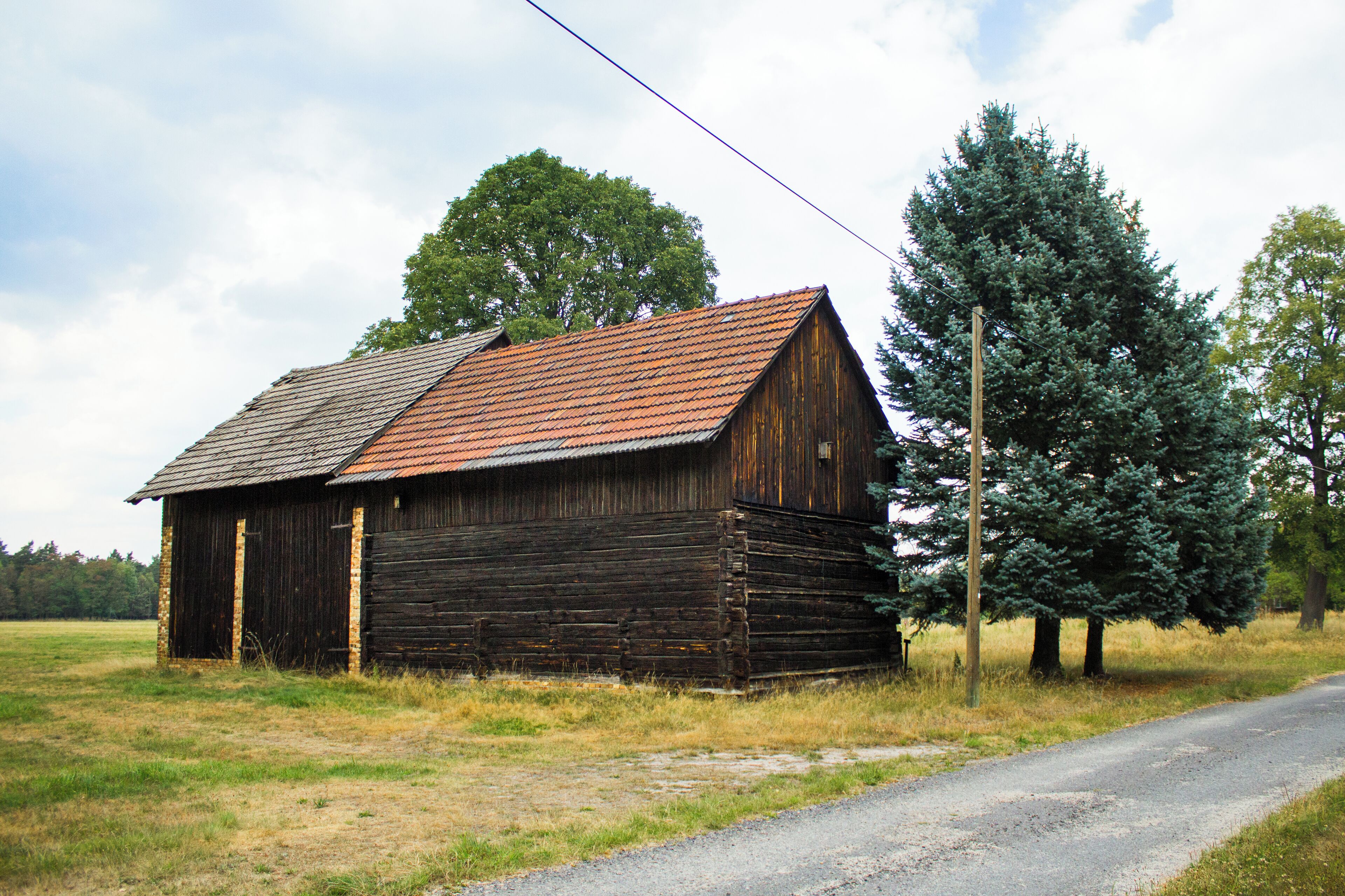 A rustic wooden barn with a red roof, surrounded by a grassy field and a few trees.