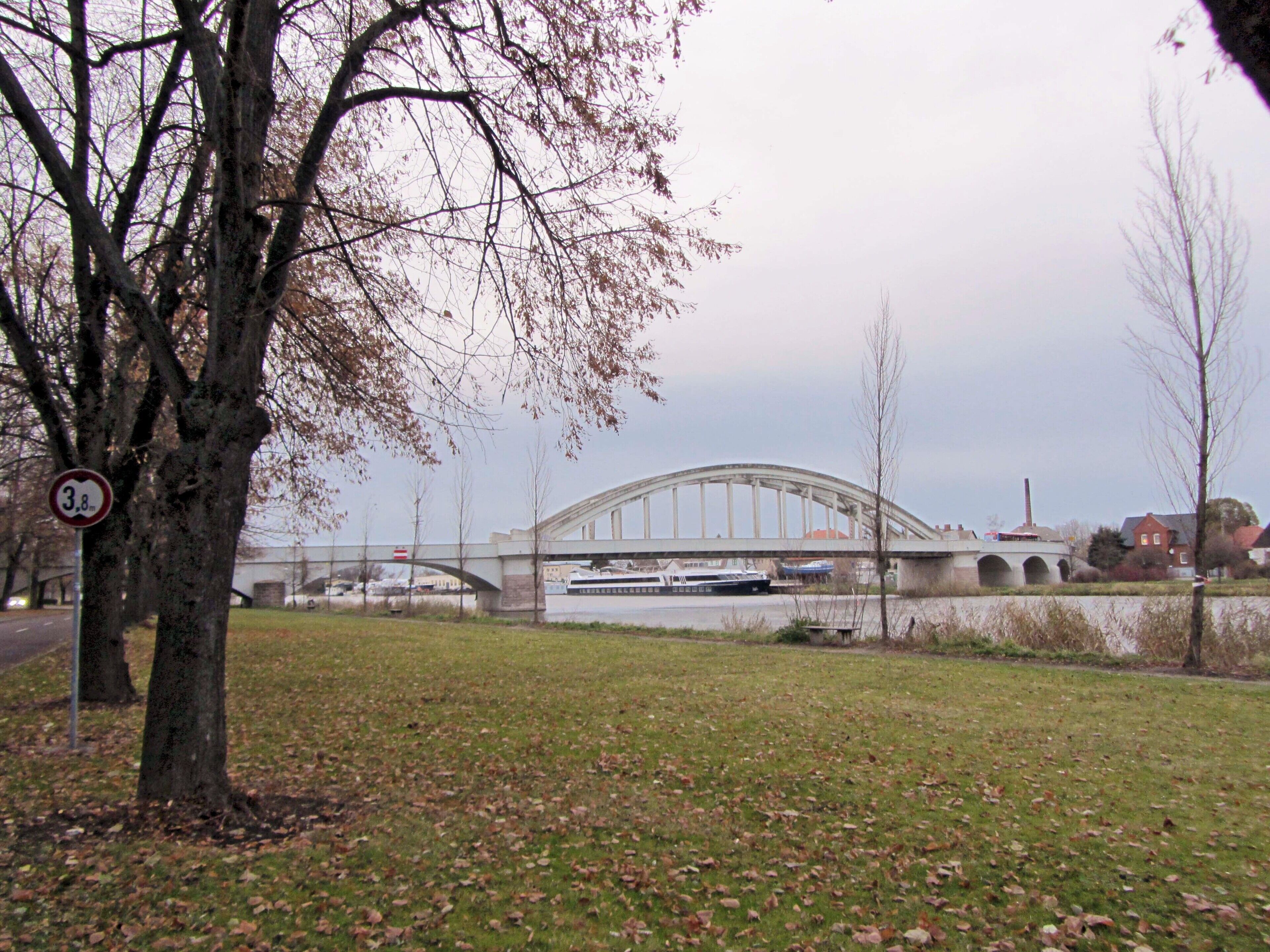 A bridge over a river, a speed limit sign, and a grassy area with trees.