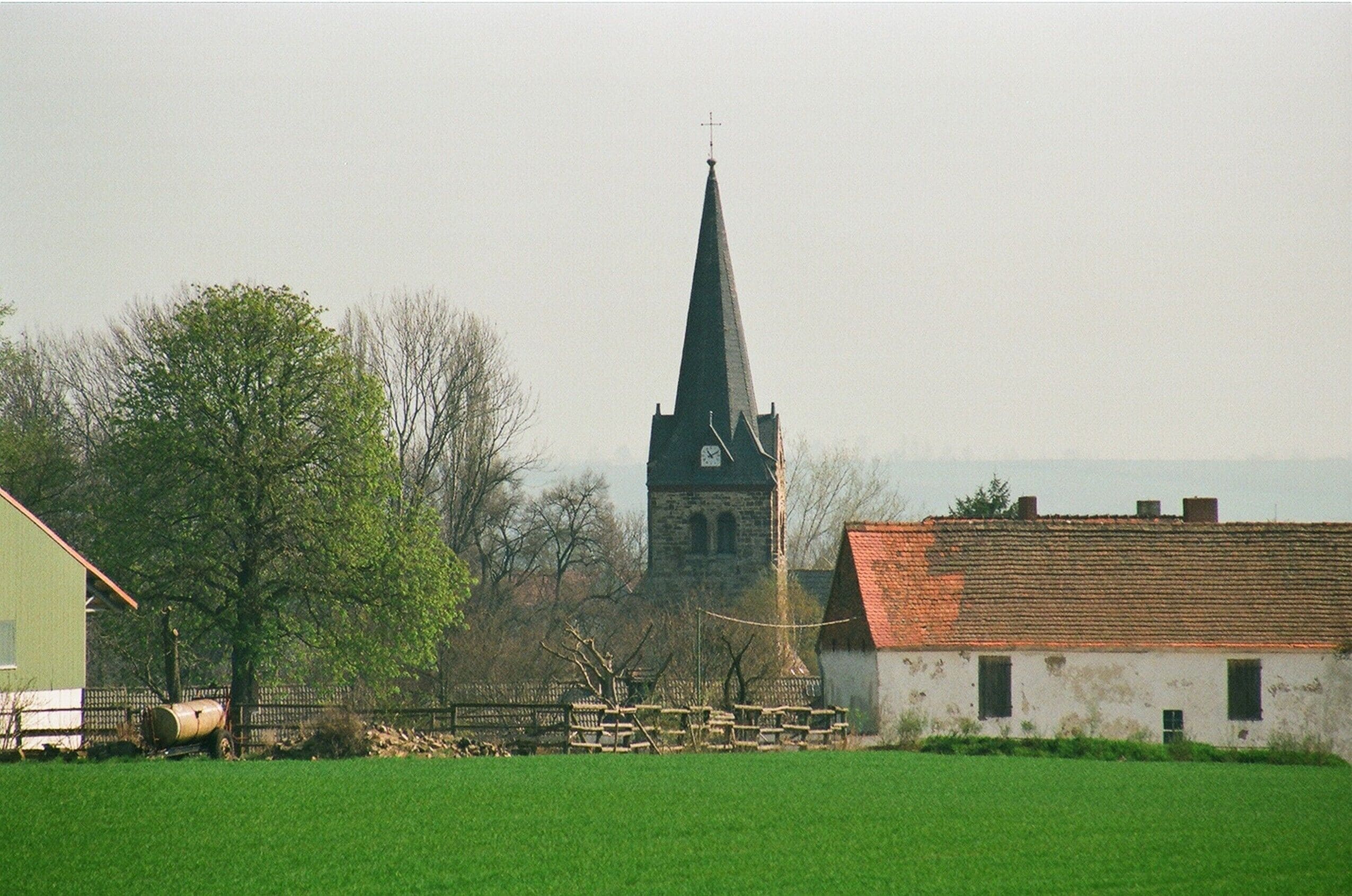 A church with a tall steeple, a green field, and a white building with a red roof.