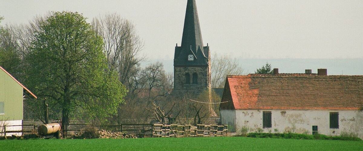 A church with a tall steeple, a green field, and a white building with a red roof.