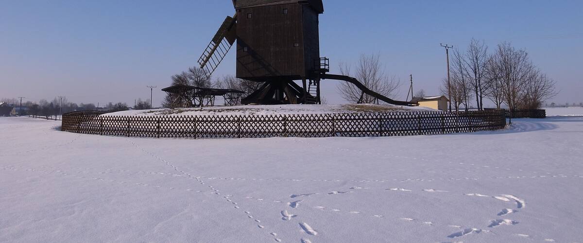 A wooden windmill in a snowy field with a fence around it.