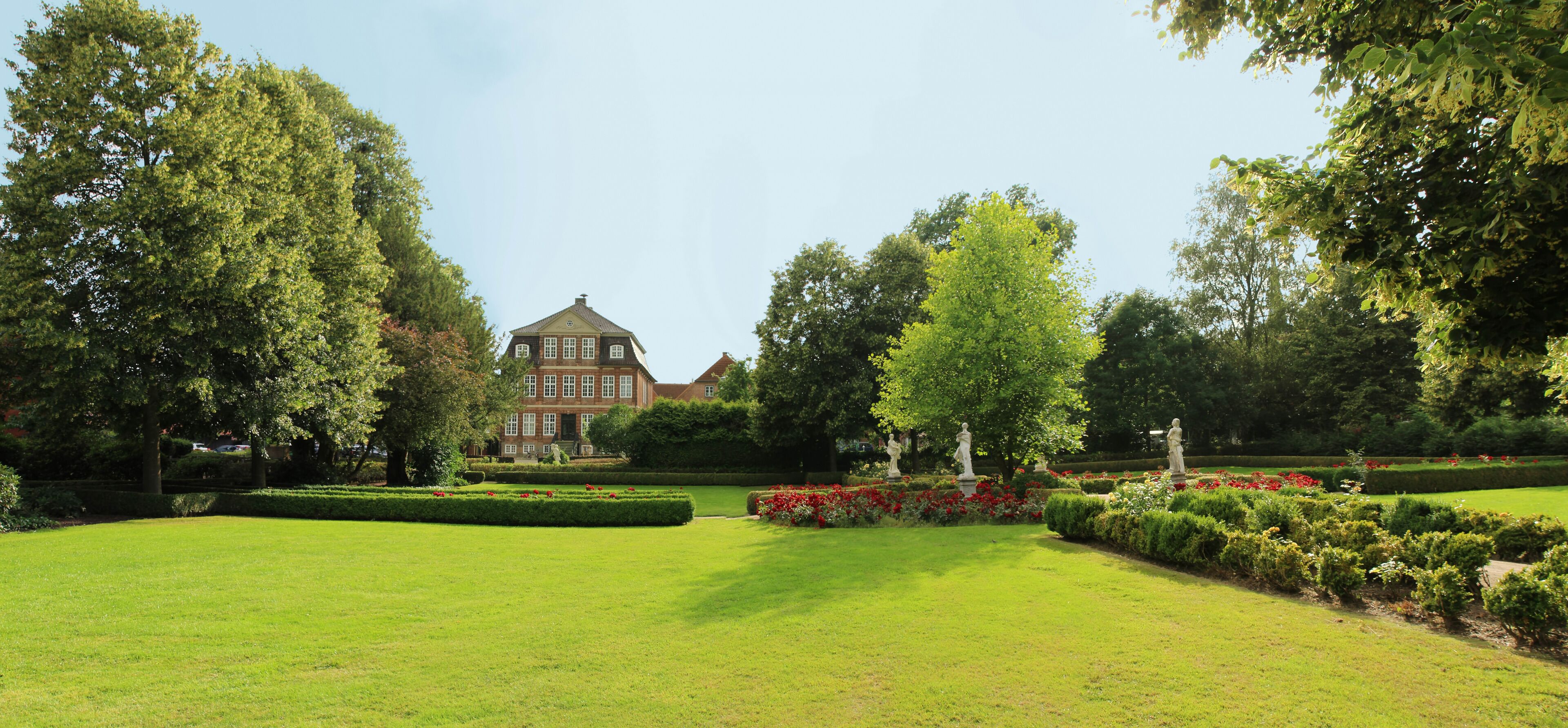 A large, historic building surrounded by well-maintained gardens and trees.