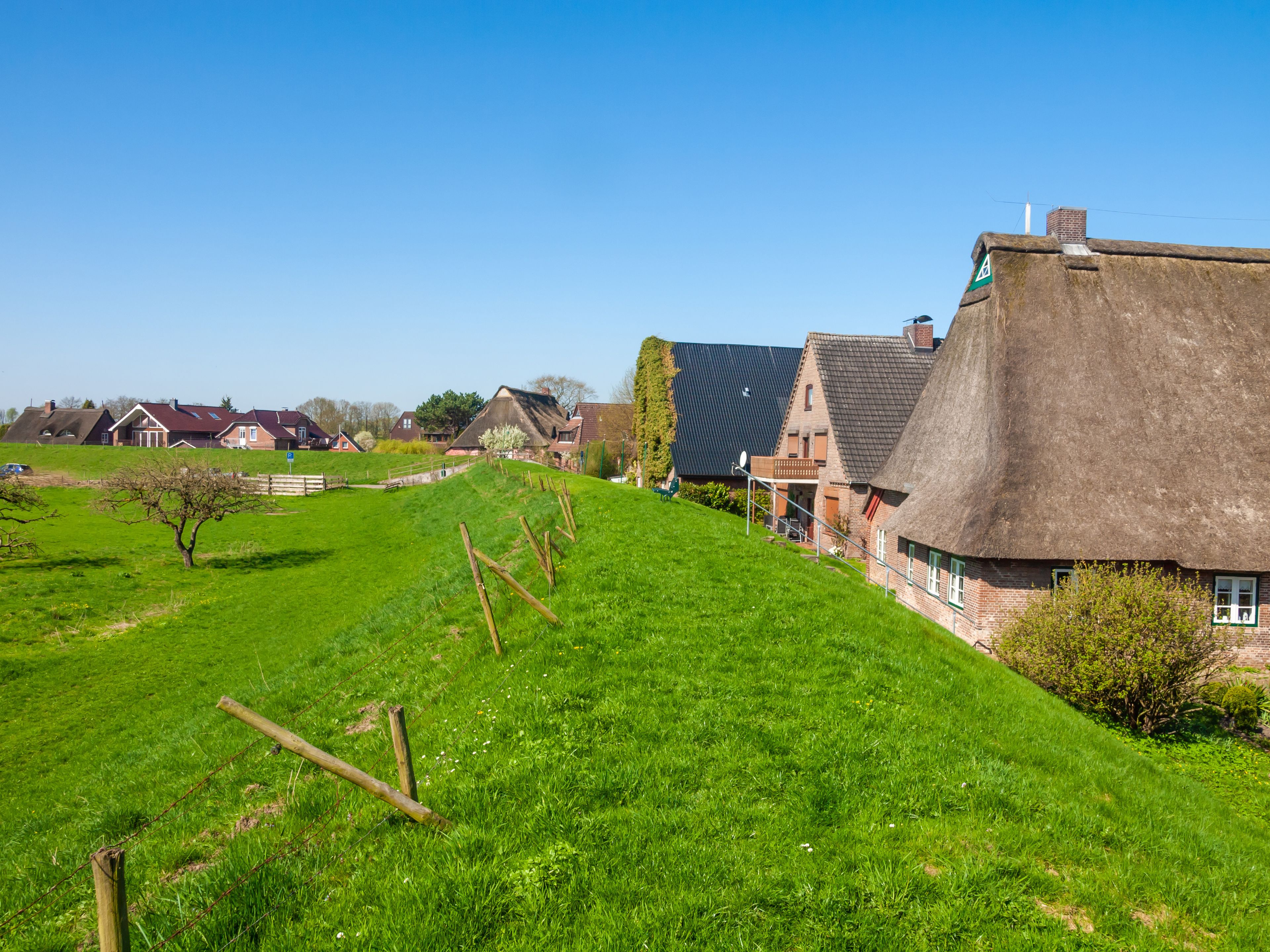 Un paisaje rural con una casa de techo de paja, campos verdes y edificios tradicionales.