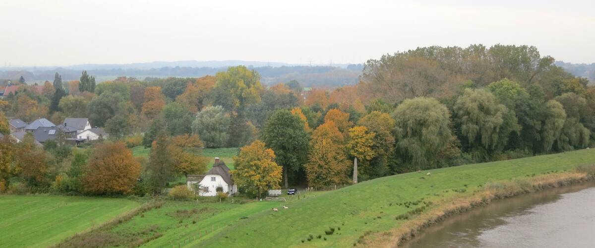 A rural landscape with a river, rolling green fields, and autumn-colored trees.