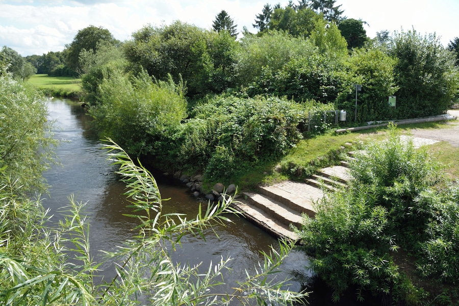 A river with a stone bridge, surrounded by lush greenery and trees.
