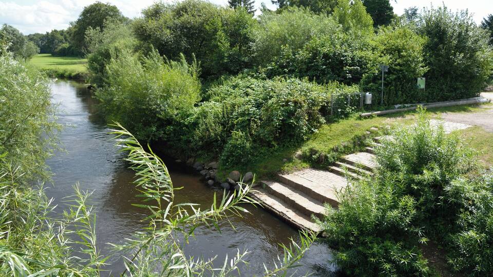 A river with a stone bridge, surrounded by lush greenery and trees.