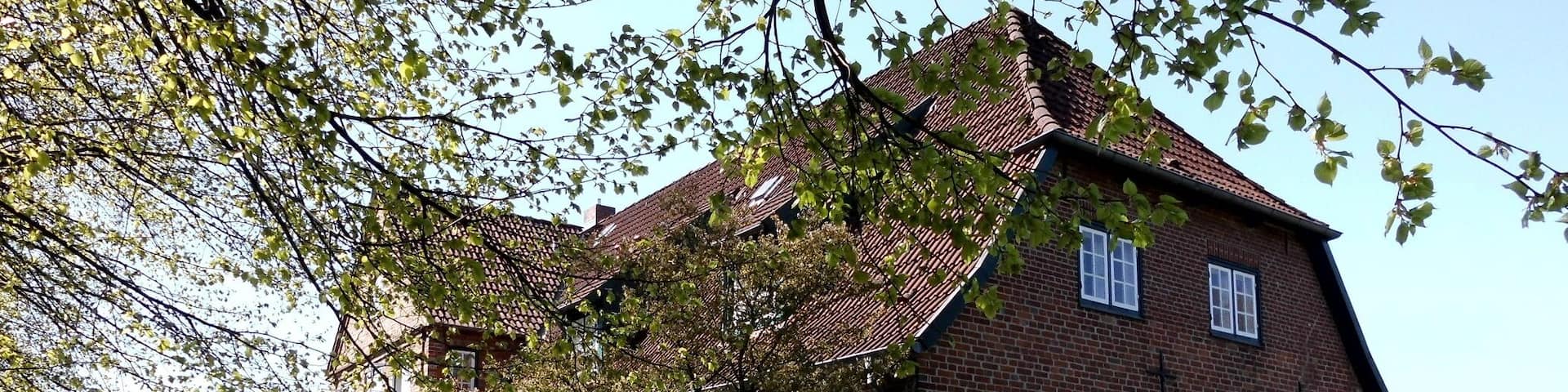 A brick church with a steep roof and a cross on the front wall, surrounded by a well-maintained lawn and trees.