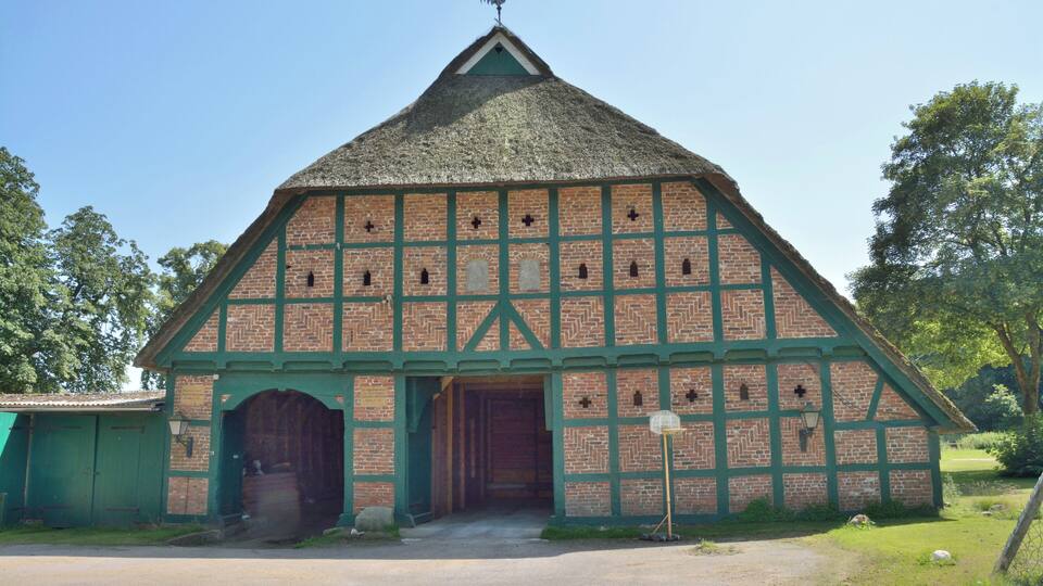 A traditional half-timbered building with a thatched roof, green accents, and a weather vane.