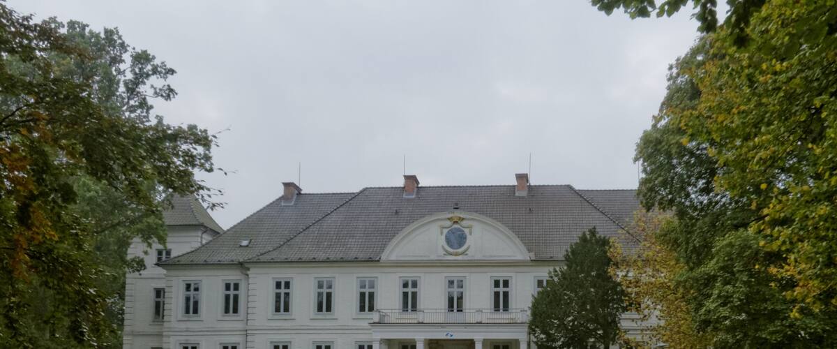 A large, white building with a symmetrical facade, a central entrance, and a formal garden with a gravel path.
