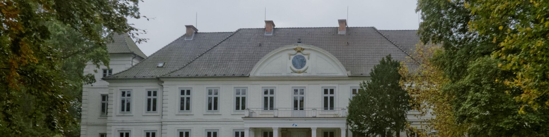 A large, white building with a symmetrical facade, a central entrance, and a formal garden with a gravel path.