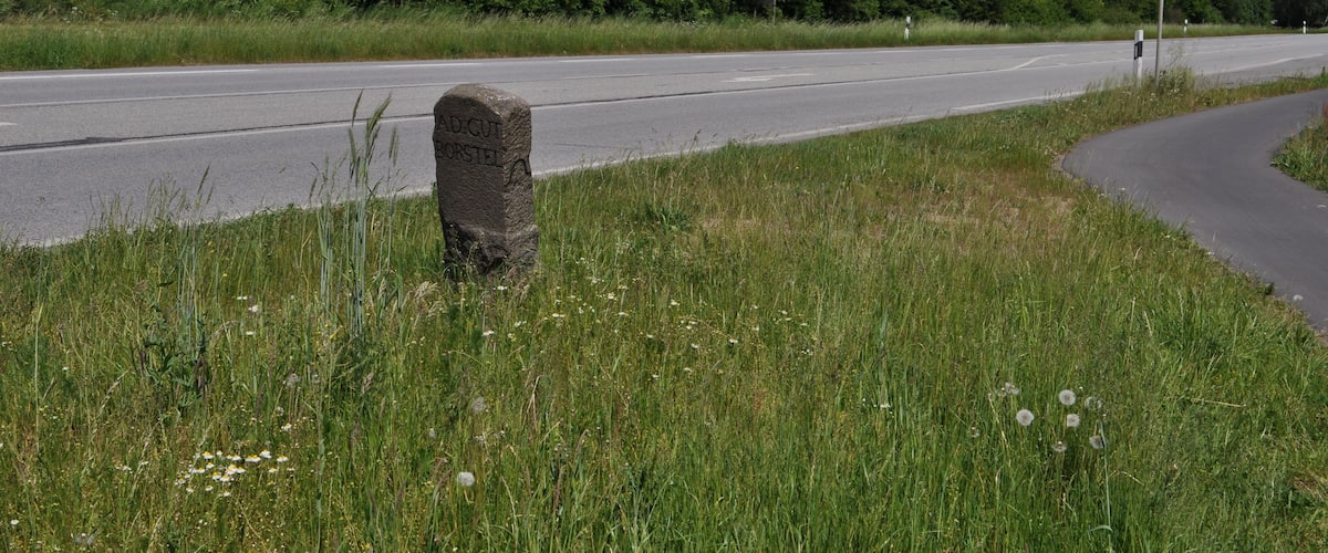 A road with a stone marker and a warning sign.