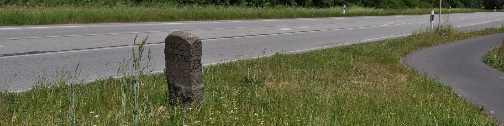 A road with a stone marker and a warning sign.