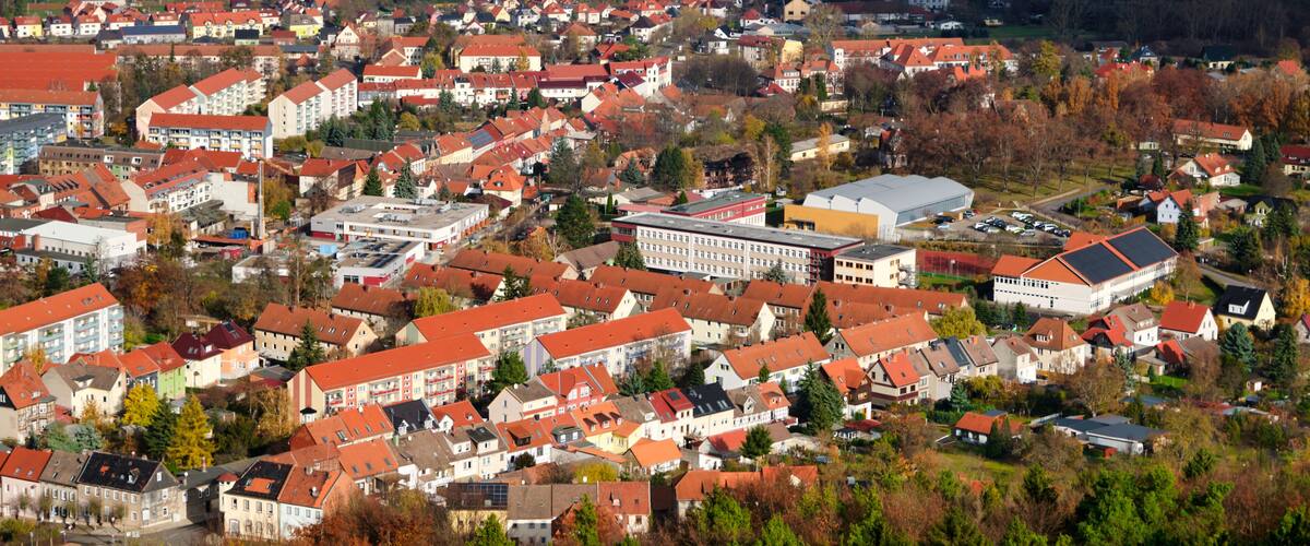 A town with red-roofed buildings, green fields, and a large white building in the center.