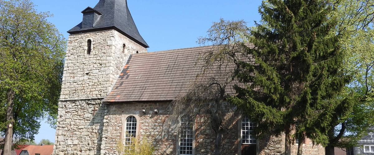 A stone church with a tall steeple and a tiled roof.