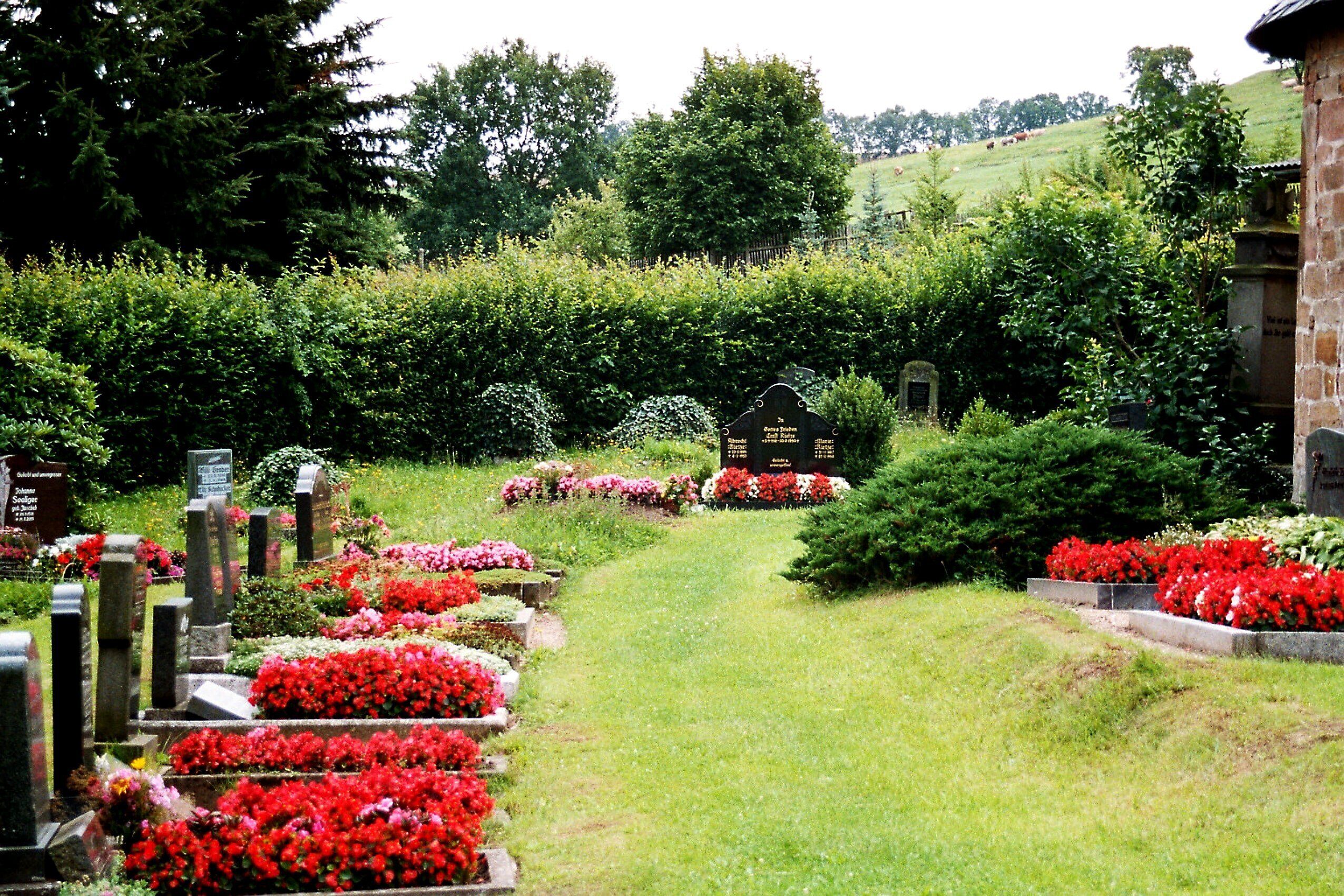 A cemetery with rows of headstones and vibrant flower beds.