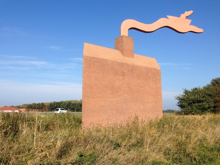 This "Monument Noordoostpolder" is a kind reminder to highway motorists about how much below sea level they are actually -safely- driving. The wave from the chimney also serves as a weather vane. - the ship is going against the currents and the wind. 
Making land where the sea once was, is not supposed to be easy. #highway-art
http://www.flevolanderfgoed.nl/home/kunst/noordoostpolder/nagele/monument-noordoostpolder.html