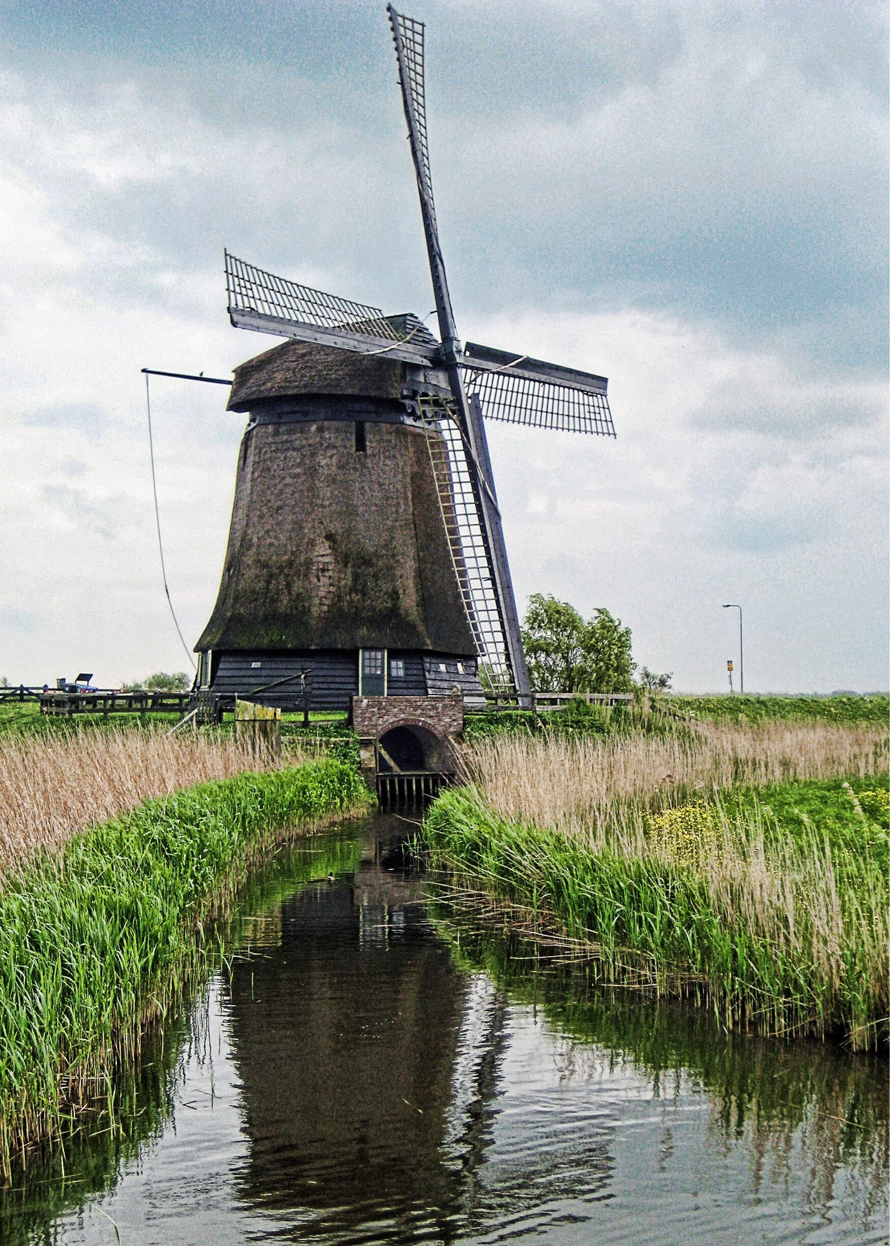 A traditional windmill by a canal with surrounding greenery.