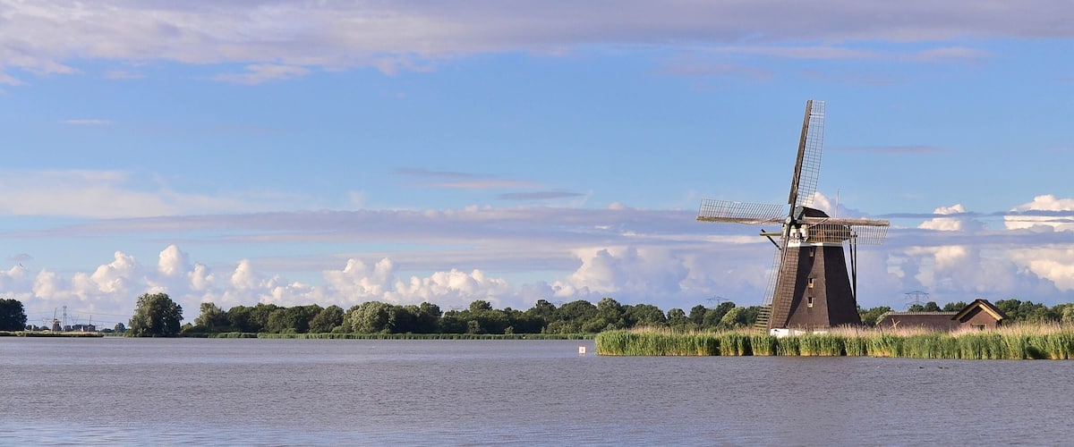 A windmill by a calm river with a clear sky.