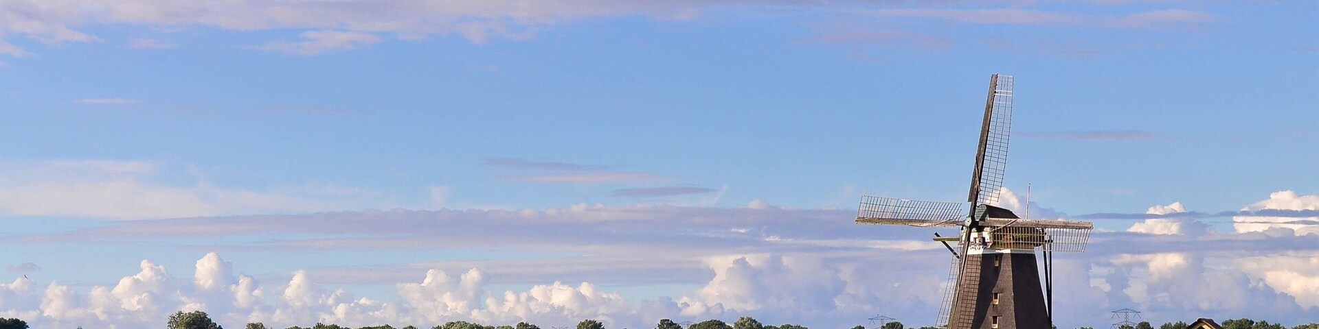 A windmill by a calm river with a clear sky.