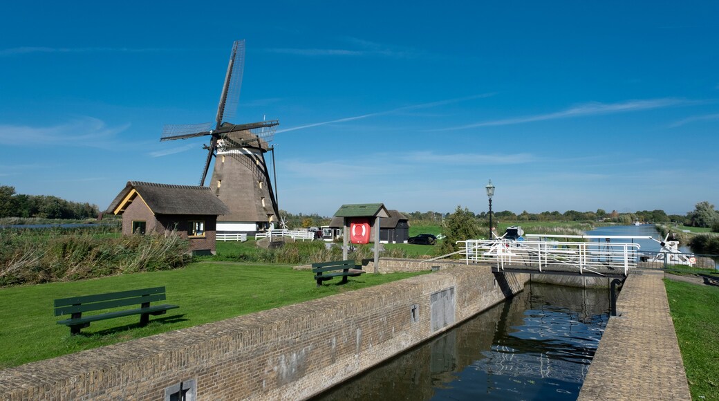 A traditional windmill, a canal, and a small building with a thatched roof.