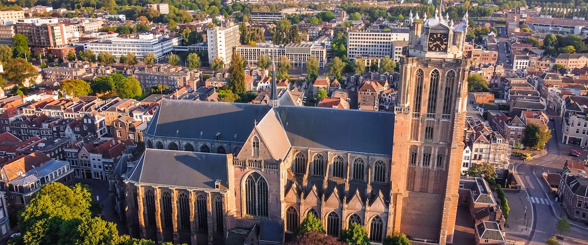Een historisch kerkgebouw met gotische architectuur, omgeven door een dichtbebouwd stedelijk gebied met moderne gebouwen en een rivier.