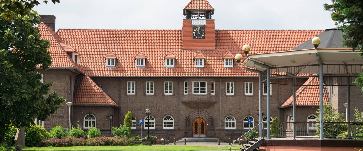 A large brick building with a clock tower, a covered walkway, and a well-maintained lawn.