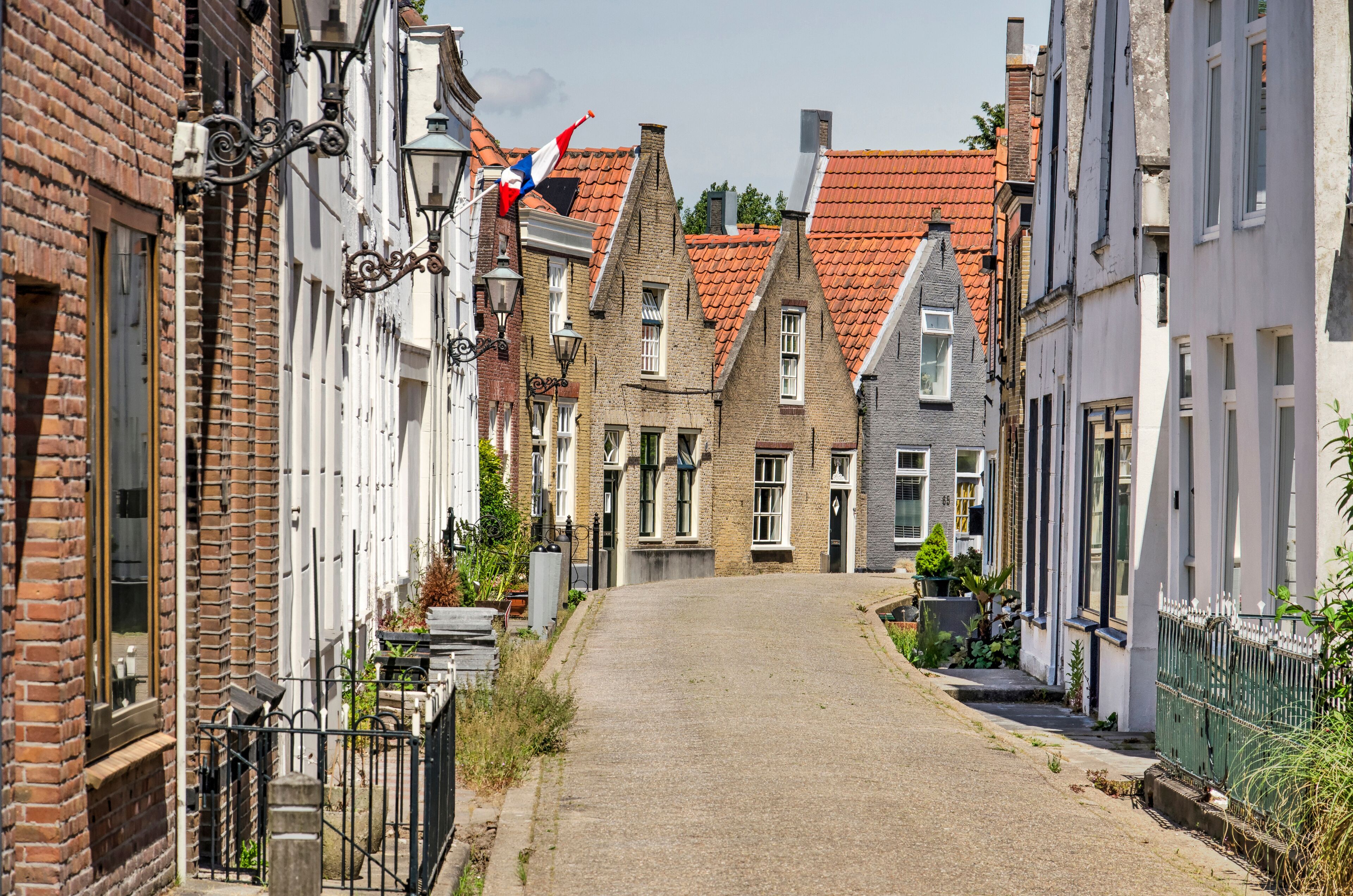 A narrow cobblestone street lined with traditional European buildings, some with red-tiled roofs and others with white facades.