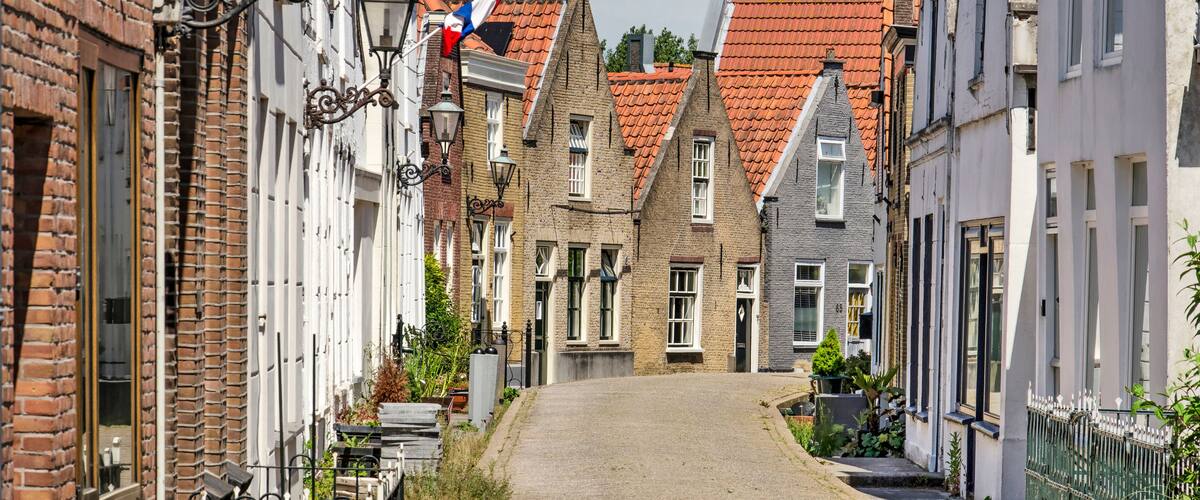 A narrow cobblestone street lined with traditional European buildings, some with red-tiled roofs and others with white facades.