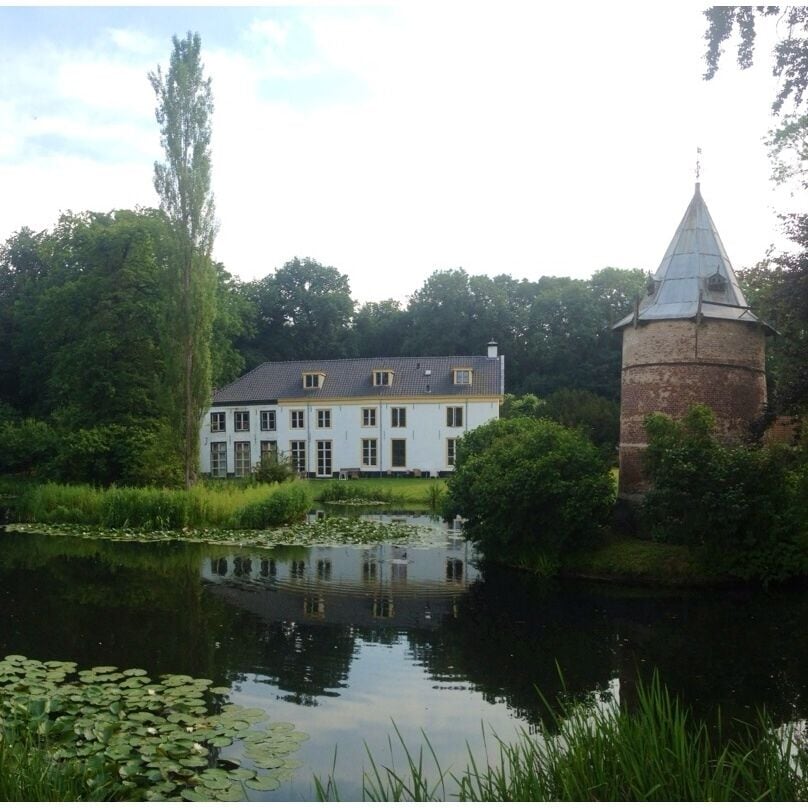 A white building with a tower, surrounded by a pond with lily pads and greenery.