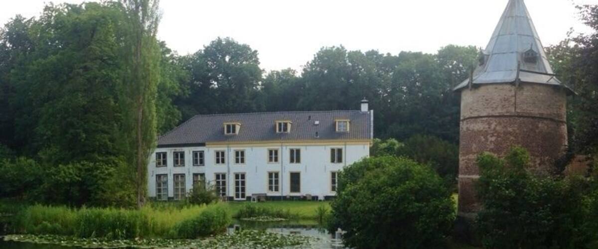 A white building with a tower, surrounded by a pond with lily pads and greenery.